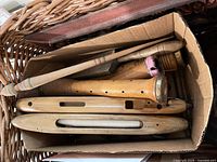 Cardboard box inside wicker basket showing multiple wooden weaving loom shuttles and tools