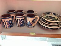 Six mugs and stack of six plates on shelf showing patterns and quantity