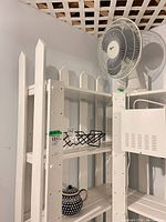 All items on shelving: white fan, black organizer, blue teapot
