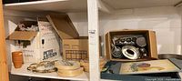 Shelf with terracotta pots, cardboard boxes containing figurines, and stack of round wooden cheese boxes