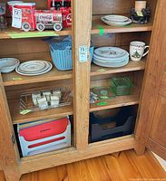 Cabinet showing stacks of dinner plates, mug, green glass container, candle holder