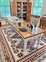 Full view of two-tone farmhouse dining table showing stained top, white legs, and scale relative to chairs and rug