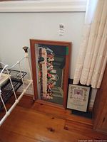Both framed pieces leaning against wall beside bed