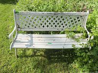 Full front view of white garden bench showing cast iron lattice back, wood slat seat and wear