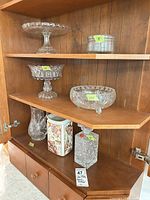 Cabinet view showing cake stand, compote, crystal bowl, porcelain canister, crystal decanter and hobnail jar