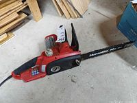 Left side view of red Homelite chainsaw showing full bar, chain, body, and cord