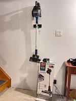 Full view of Hoover ONEPWR Blade+ stick vacuum mounted on wall with box and battery charger below