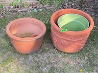 Two terracotta planters side by side outdoors; right pot contains green plastic liner