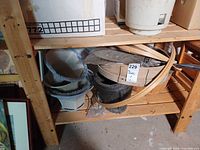 Shelf with three stacked fabric lamp shades, black feed bucket, wooden apple basket, embroidery hoops