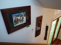 Framed Maud Lewis print, wood plaque, metal bell on wall