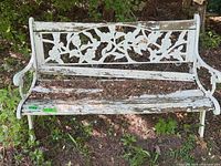 Front view of entire white cast iron garden bench showing peeling paint and ornate floral back