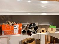 Shelf with shoe box of taper candles, multiple rolled posters and wallpaper rolls