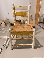 Front view of ladderback wood chair showing overall form, paint wear, and woven seat