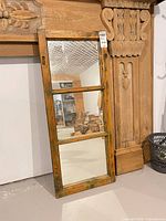 Full view of rustic three-pane wood framed mirror leaning against wall