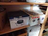 Two boxed raclette grill sets on shelf highlighting T-fal box front and side