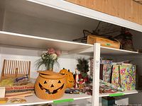 Shelf view showing ceramic and plastic jack-o-lanterns, wooden rack, Noah’s Ark toy, artificial greenery, twig star, Santa figurine, gift wrap and bags