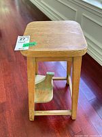 Overall view of wooden backless stool showing seat, legs, and hinged foot platform