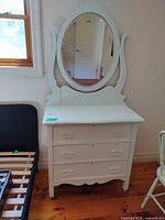 Front view of white dresser with three drawers and attached oval mirror