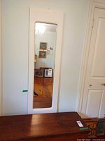 Frontal view of full-length mirror on wall showing white wood frame and reflective glass