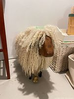 Full view of sheep sculpture showing wool fleece body, wood head and legs, metal bell