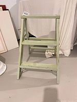 front view of light green wooden two-step ladder showing overall condition and paint wear