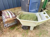 Yard cart filled with grass clippings beside two bags of soil/mulch