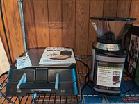 Waffle maker closed with manual on lid, coffee grinder beside it