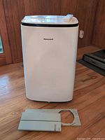 Front view of Honeywell portable AC with remote on top and window kit panel on floor