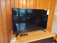 Front view of Insignia TV on stand with remote placed in front