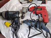 Overview of three corded drills and right-angle attachment on tarp