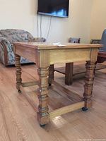 Full view of oak end table showing turned legs, stretcher and casters