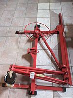 Folded red steel drywall lifter panel hoist with winch and caster wheel visible