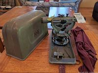 Overall view of theodolite mounted on base beside hard metal case