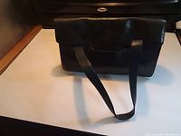 Front view of black pebbled leather shoulder bag showing flap and straps