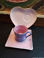 Cup set on square saucer, heart saucer behind, showing colors and silver rims
