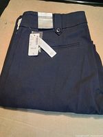 Folded dark navy trousers with waistband, pocket, and attached price tag visible