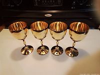 Four gold goblets in a row showing reflective finish and monograms