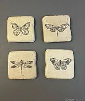 Four beige ceramic coasters with insect illustrations