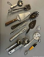 All twelve assorted vintage serving utensils laid out on flat surface