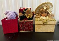 Three decorative boxes with figurines: purple rabbit, teddy bear, porcelain doll