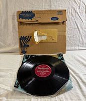 Vinyl record displayed in front of cardboard mailer and envelope