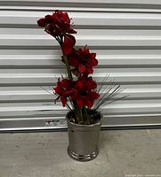 Full view of artificial amaryllis arrangement showing red flowers, stems, foliage, and silver pot