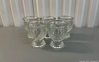 Group of five clear glass votive candle holders showing pattern and pedestal bases