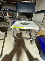 Front view of aluminum commode chair showing blue backrest, armrests, white seat insert and casters