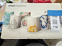 Top of Cricut Mug Press box displaying brand name and decorated sample mugs