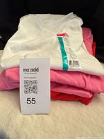 Stack of folded T-shirts showing white, pink and red colors with lot tag