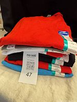 Stack of eight folded Gildan T-shirts showing assorted colors and attached tags