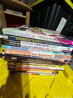Stack of 15 paperback manga/anime drawing books on yellow tote