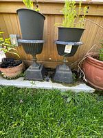 Pair of black composite pedestal urns with plastic pots inside, front view