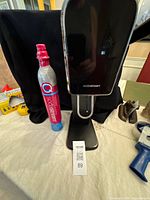 Front view of black SodaStream maker standing next to pink Quick Connect CO2 cylinder